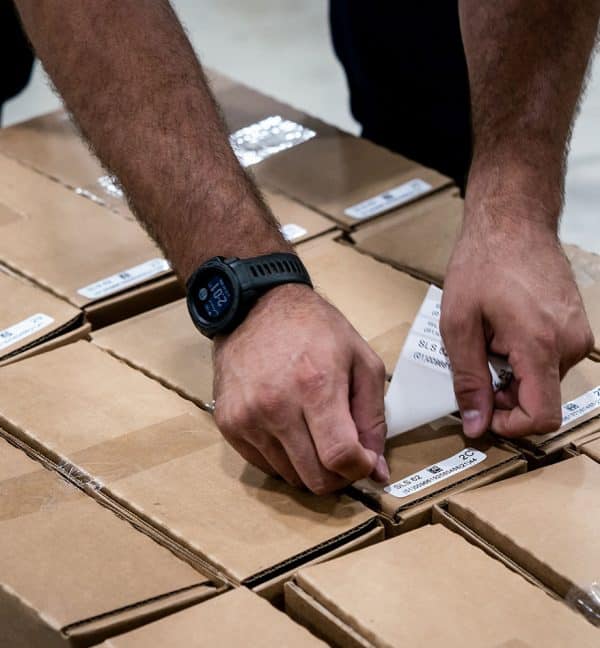 un homme colle des etiquettes adhésives avec code barre sur des cartons dans un entrepot supply chain