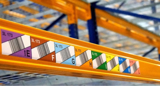 Dans un entrepôt des racks oranges avec des etiquettes durables imprimes codes barres et lettre couleur des allées