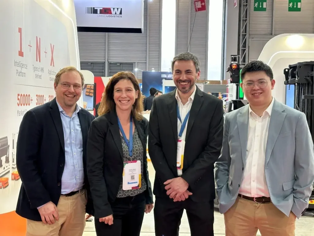 Partenariat-HIKRobot-SITL-2024 Quatre personnes souriantes à un salon professionnel, présentant des solutions durables. WIIO et Hikrobot collaborent en France.