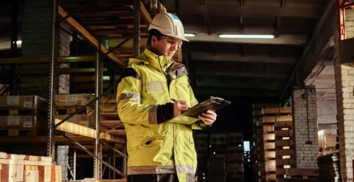 Ouvrier avec casque et clipboard dans un entrepôt, assurant la conformité de la chaîne du froid avec l'IoT.