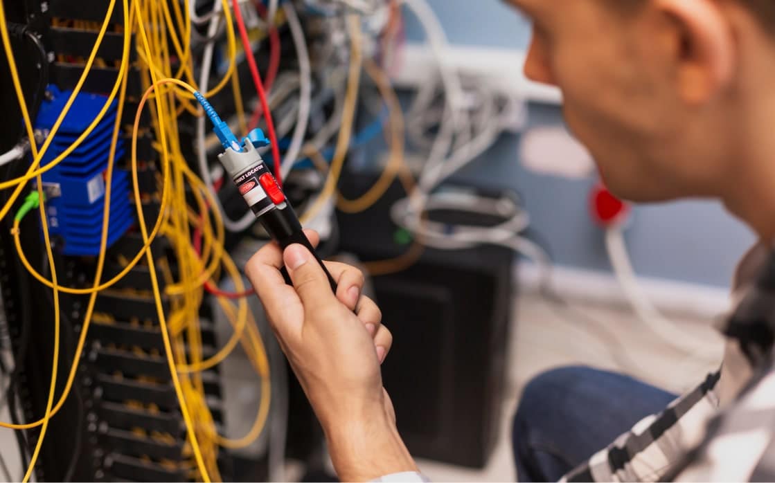 Technicien utilisant un localisateur visuel de défauts sur fibre optique pour la gestion du parc informatique.