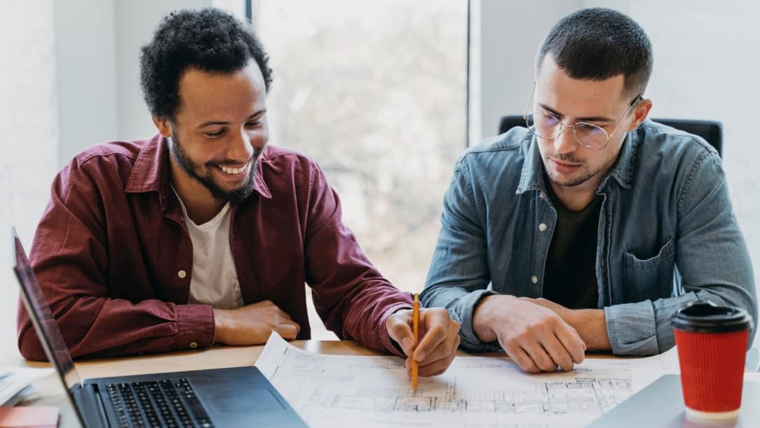 Deux hommes discutent de solutions robotiques sur un plan, avec un ordinateur portable.