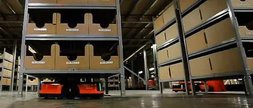 Robots AMR "pallet to person" déplaçant des étagères dans un entrepôt.