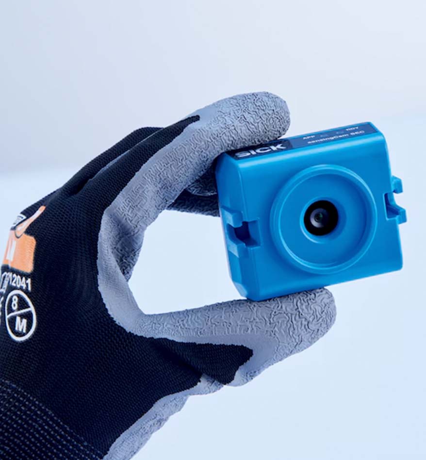 Main tenant un SensingCam Sick 100SEC bleu. Capteur de vision industrielle.
