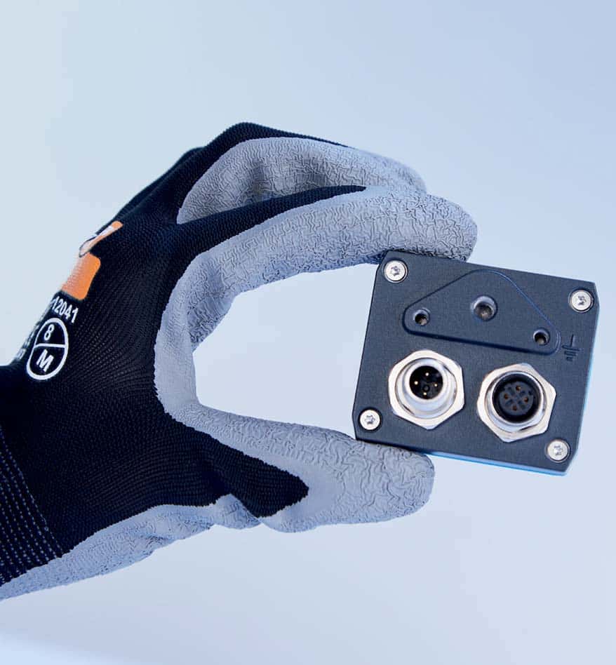 Main tenant une SensingCam Sick 100SEC. Connecteurs visibles.