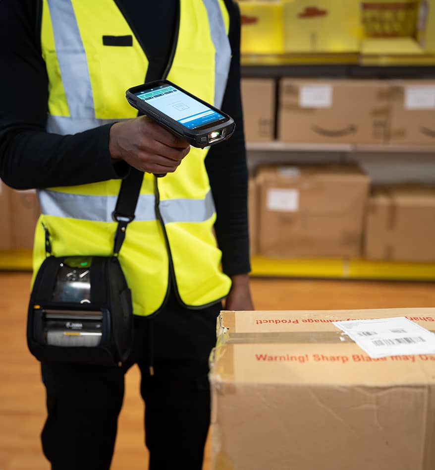 Employé scannant un colis avec un terminal mobile Zebra TC22 dans un entrepôt.