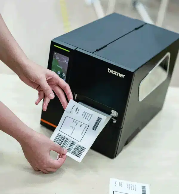 Imprimante industrielle Brother TJ-4121TN imprimant une étiquette, avec une main retirant l'étiquette.