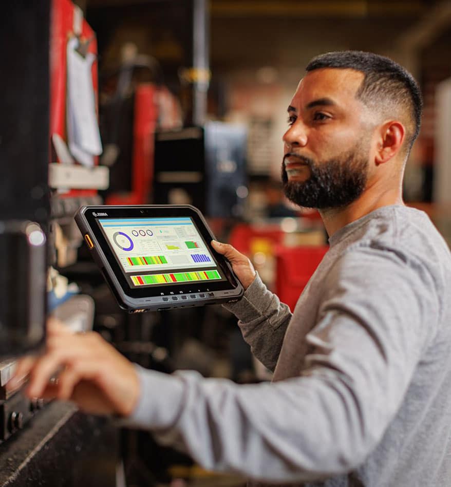 Ouvrier utilisant une tablette durcie Zebra ET60 dans un entrepôt. Écran avec des graphiques affichés.
