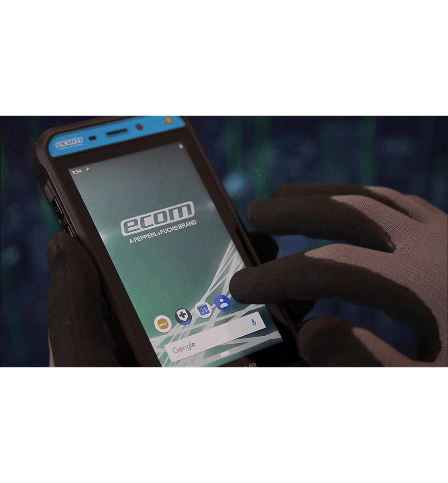 Terminal ATEX Smart-Ex 02 DZ1 ECOM utilisé avec des gants. L'écran affiche le logo ECOM.