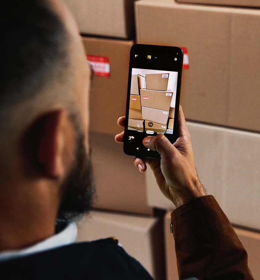Homme photographiant des cartons avec un terminal mobile RFID Zebra EM45. Inventaire logistique.