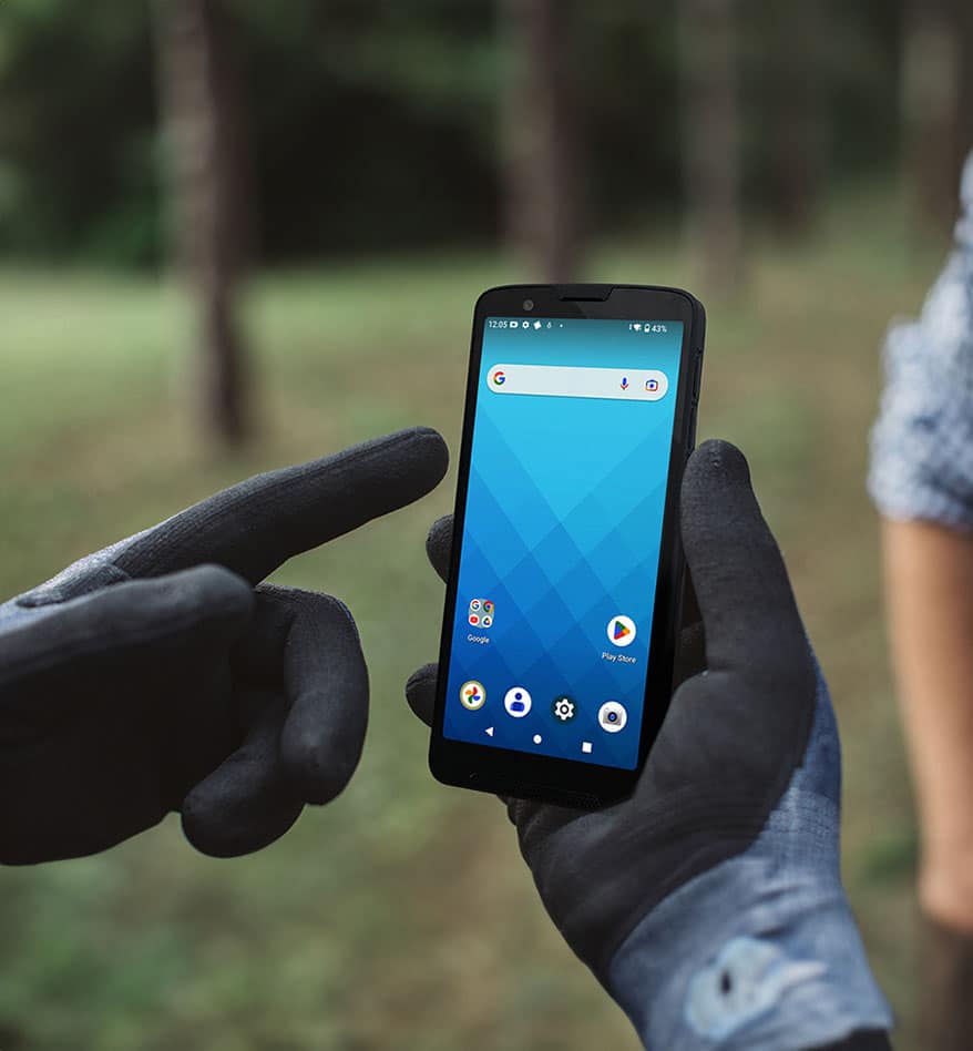 Terminal mobile Unitech EA660 tenu par des mains gantées. Écran bleu avec icônes d'applications.