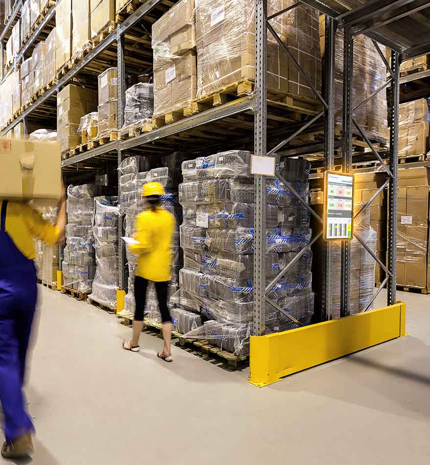 Entrepôt avec un ordinateur type kiosque Zebra KC50, employés et rayonnages remplis de marchandises.