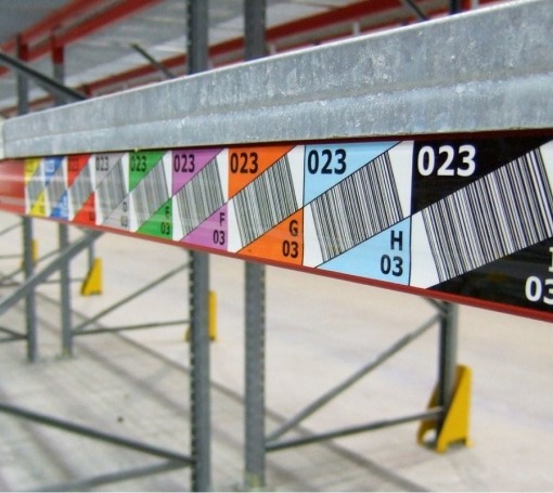 Étagères d'entrepôt avec étiquettes colorées et codes-barres pour la gestion des consommables.