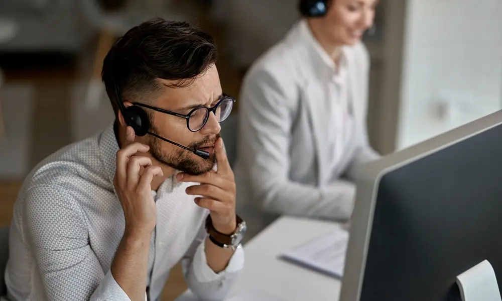 Agent de centre d'appels pensif travaillant sur des solutions robotiques avec un casque.