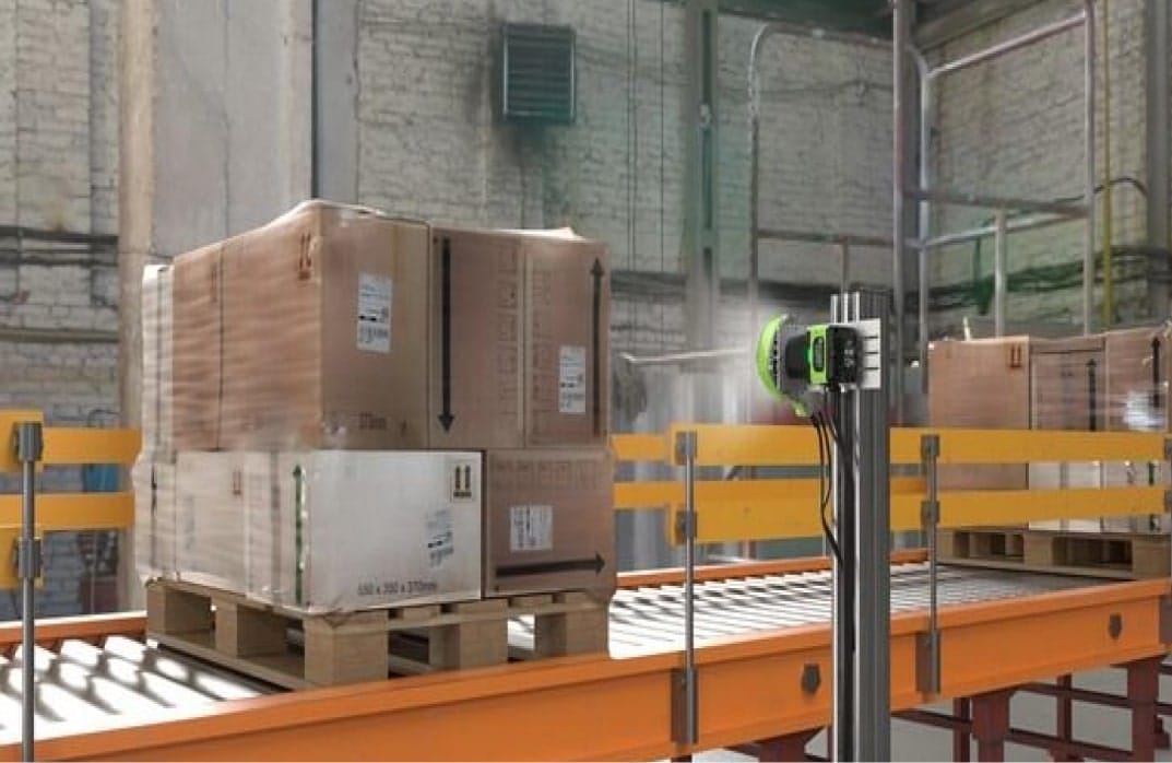 Palette de cartons sur convoyeur dans un entrepôt, illustrant la gestion de parc informatique et pilotage.