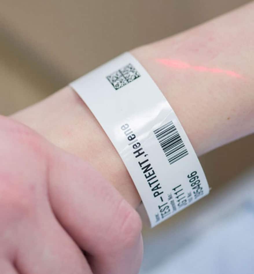 Bracelet d'identification thermique et laser sur le poignet d'un patient, avec code QR et code-barres.