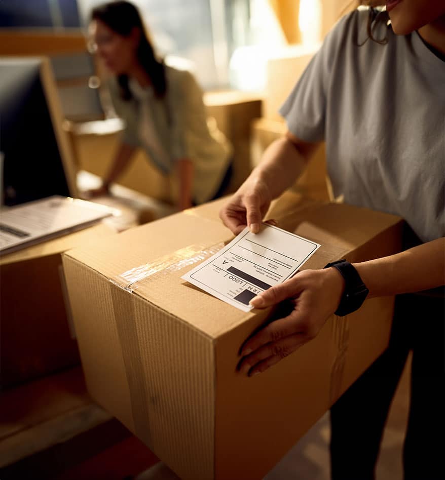 Femme appliquant une étiquette papier sur un carton. Étiquettes Papier.