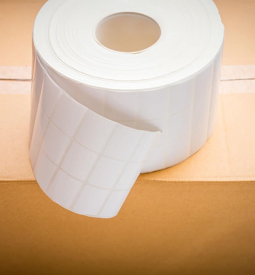 Rouleau d'étiquettes polypropylène blanches sur une boîte en carton.