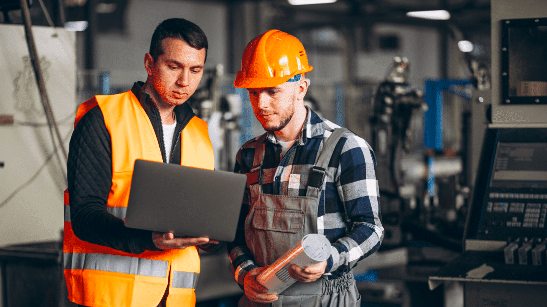 Deux ouvriers discutent des solutions métiers devant un ordinateur dans une usine.