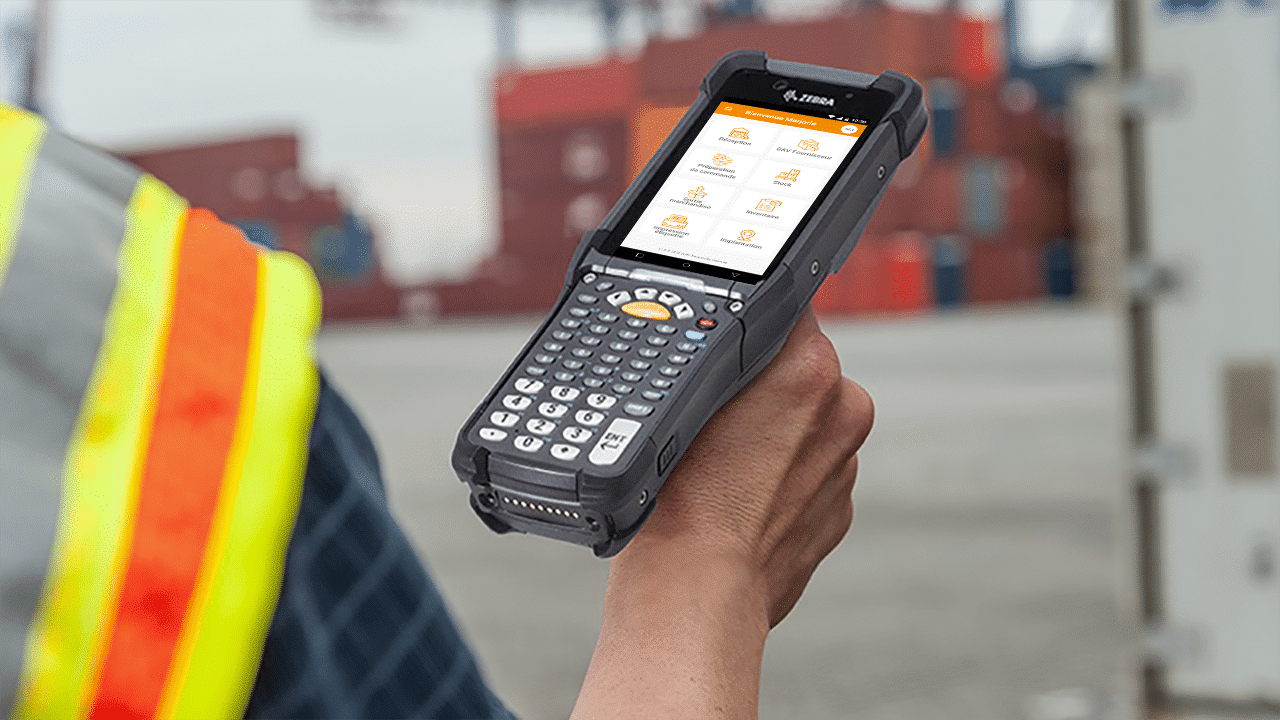 Ouvrier tenant un appareil mobile Zebra avec des solutions de gestion d'entrepôt affichées.