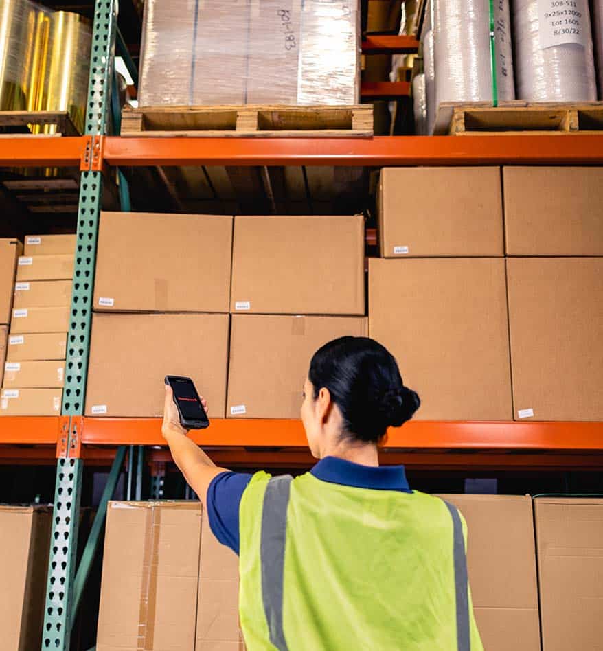 Employée d'entrepôt utilisant un terminal mobile Honeywell CT47 pour scanner des boîtes sur des étagères.