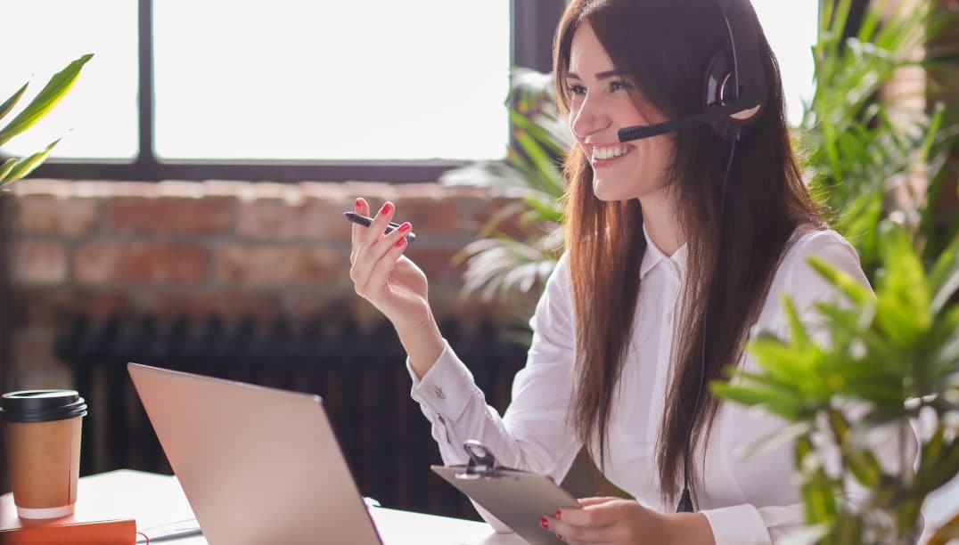 Femme souriante avec casque, travaillant sur un ordinateur portable. Services WIIO.