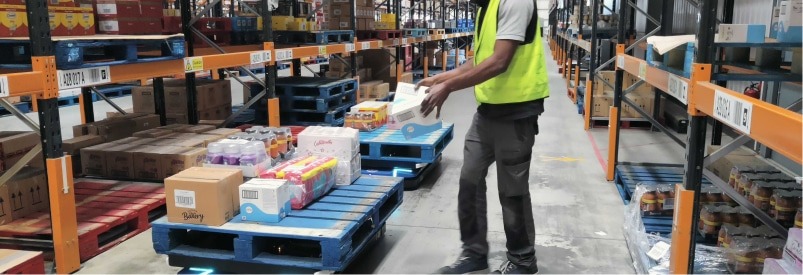 Préparation de commande : Employé plaçant une boîte sur une palette automatisée dans un entrepôt.