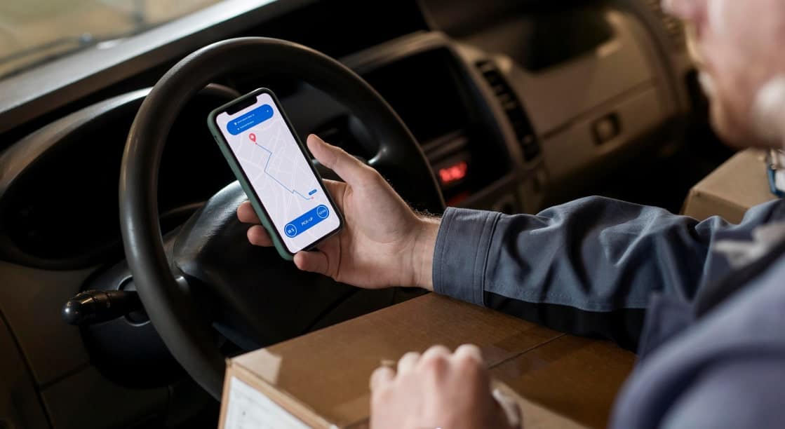 Livreur utilisant une application de gestion du transport et des flottes sur son téléphone.