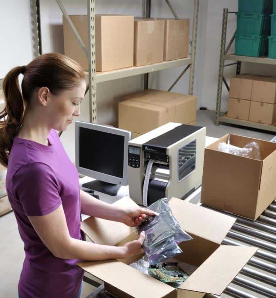 Femme emballant des produits avec une imprimante de rubans transfert thermique à proximité.