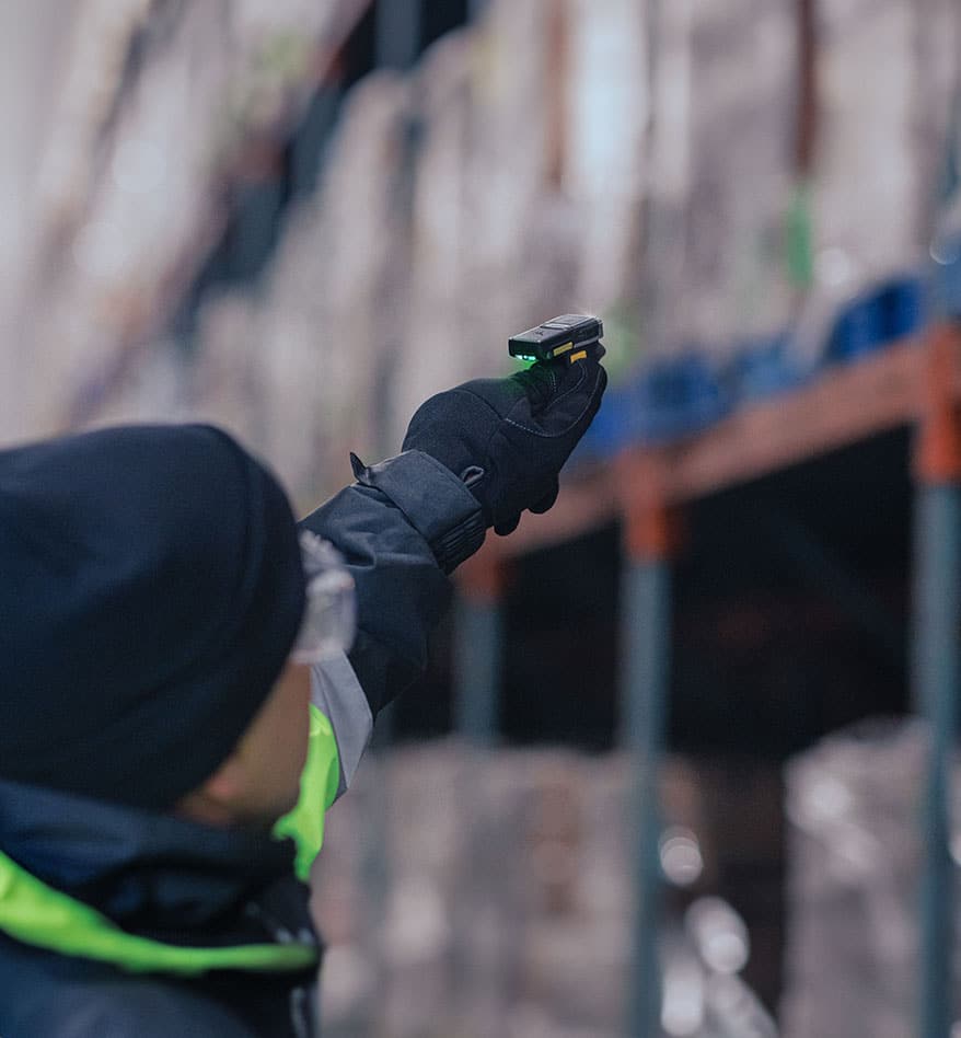 Scanner Zebra RS6100 porté par un employé dans un entrepôt, avec rayonnage flou en arrière-plan.