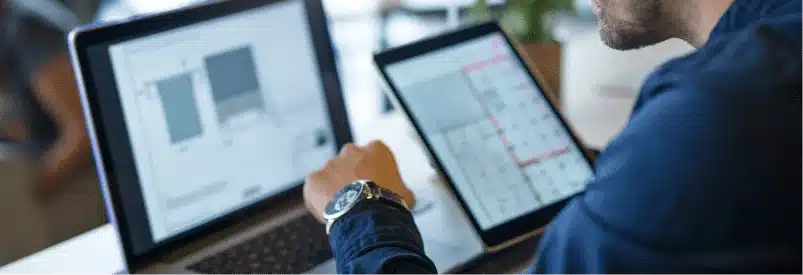 Homme consultant des solutions métiers sur un ordinateur portable et une tablette.