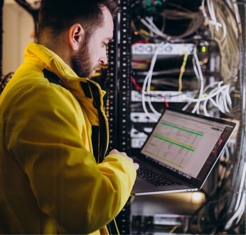 Technicien utilisant un ordinateur portable devant un serveur, pilotage et remontée des KPI.