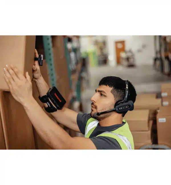 Employé d'entrepôt utilisant le terminal mains-libres Honeywell CW45 avec casque et lecteur de codes-barres au bras.