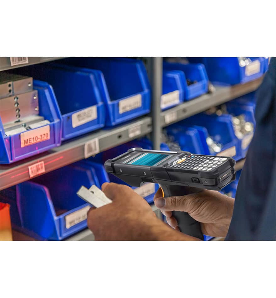 Terminal MC3300x Zebra utilisé pour scanner un code sur une étagère d'entrepôt.