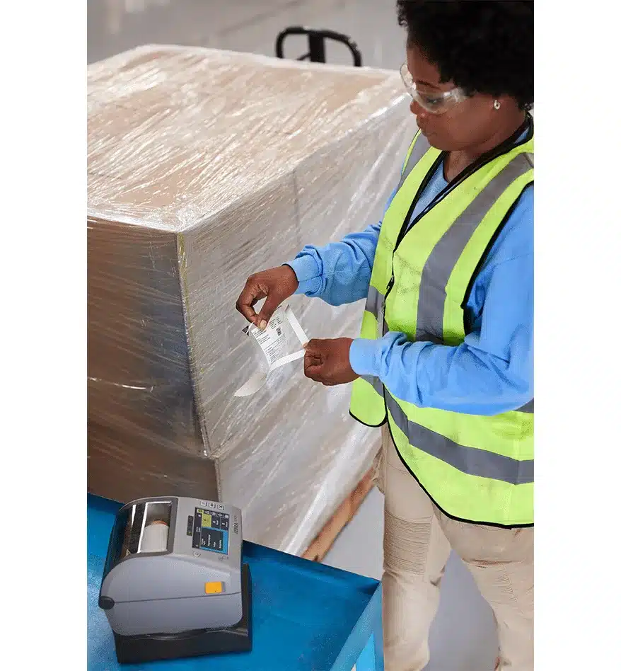 Employée apposant une étiquette imprimée par une imprimante de bureau Zebra ZD621 sur une palette emballée.