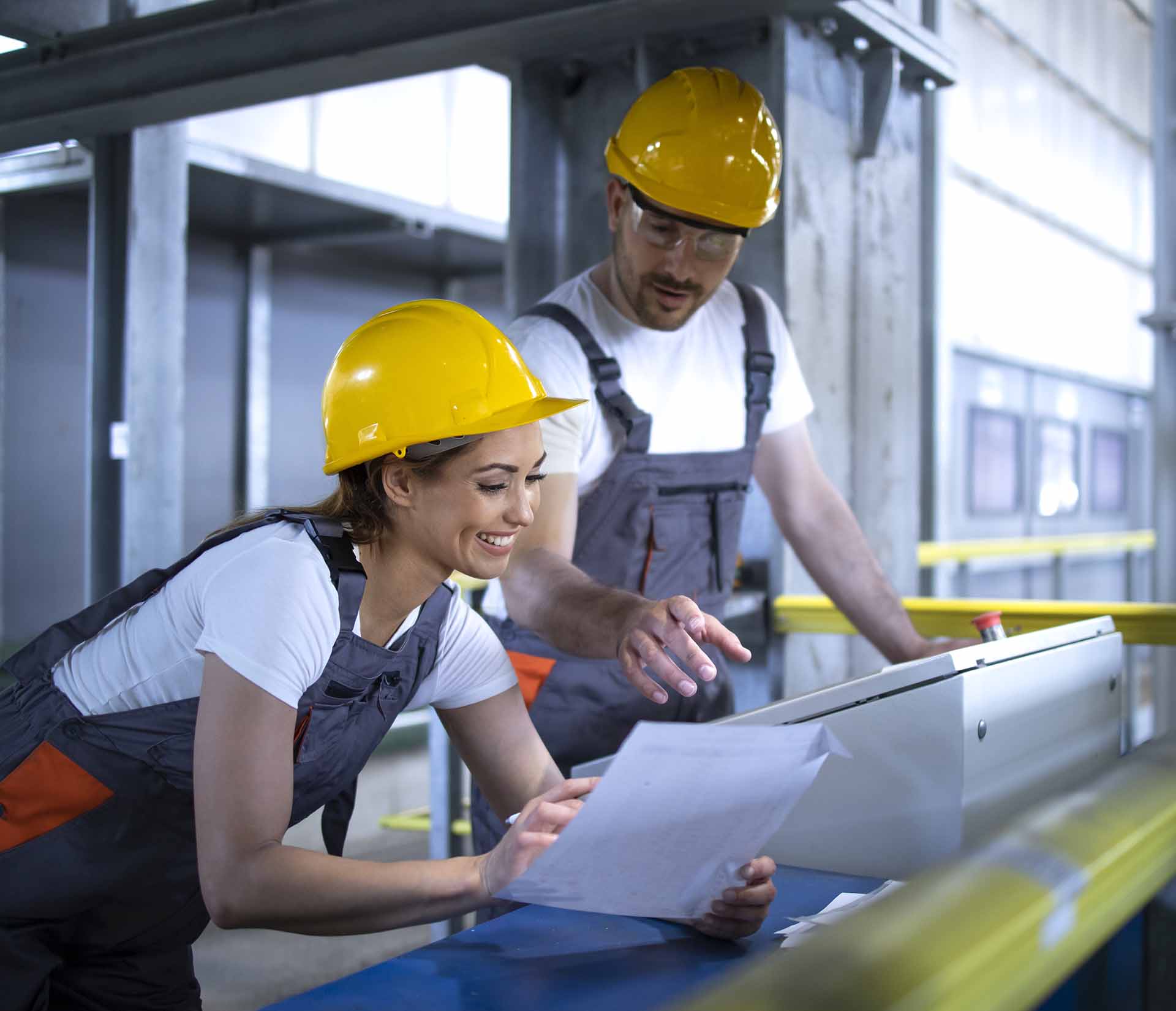 Deux ouvriers avec casques jaunes examinant des documents dans une usine. Glossaire K-Z.