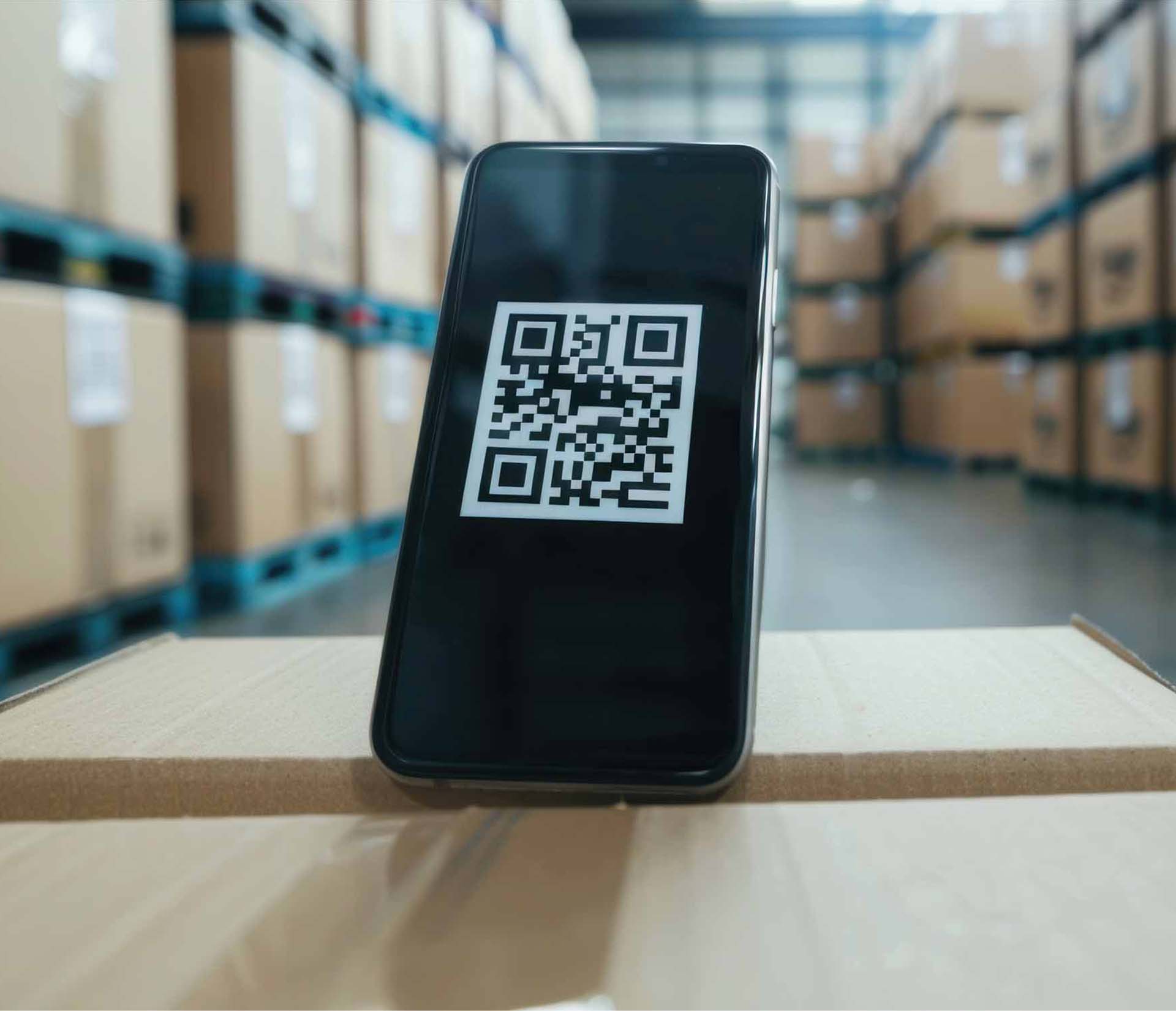 Téléphone avec un QR code sur un carton dans un entrepôt. Glossaire K-Z.