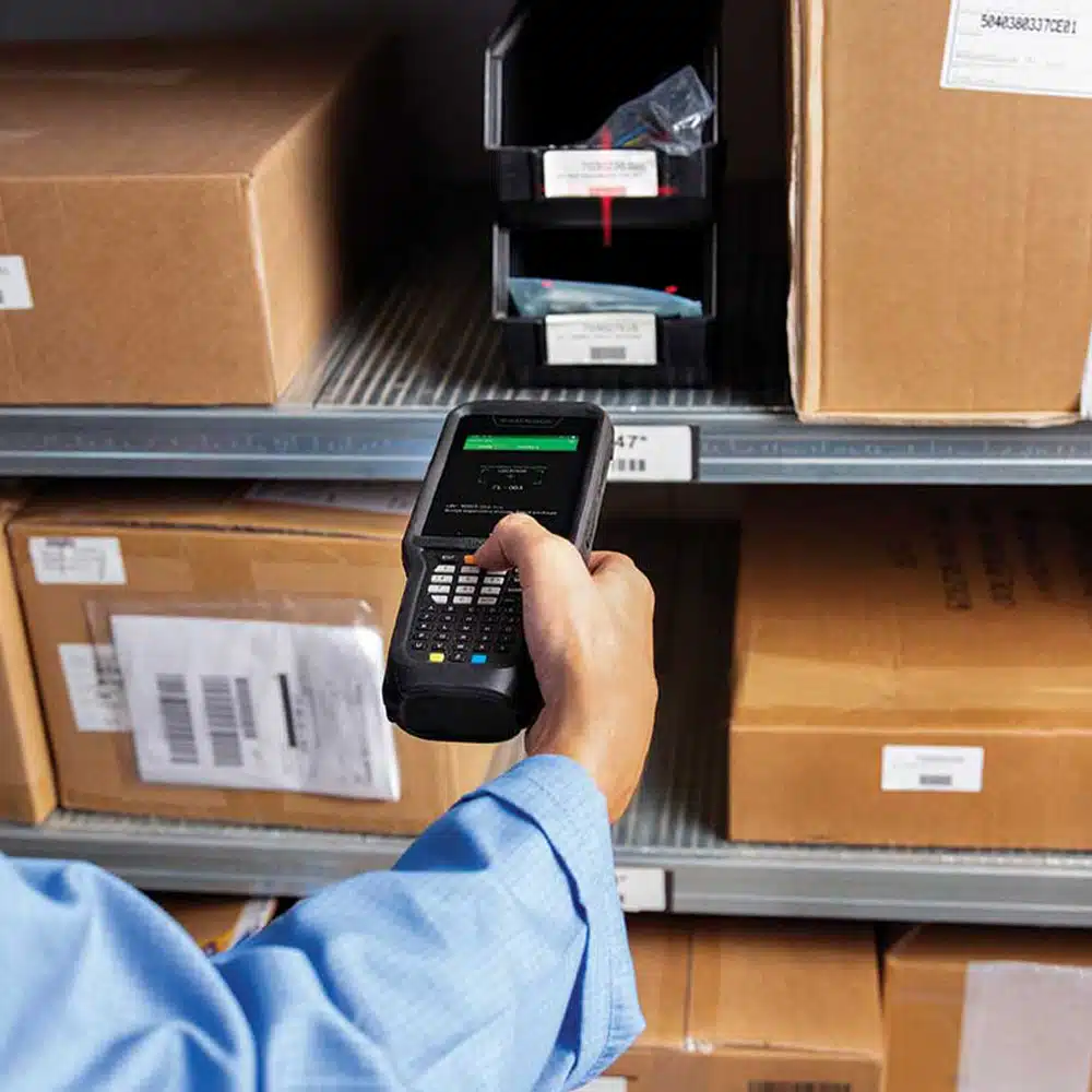 Employé scannant un code-barres avec un terminal mobile dans un entrepôt. Location matériel.